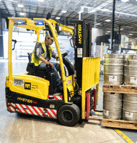 A forklift operator using the machinery to move stacked pallets loaded with metal barrels.