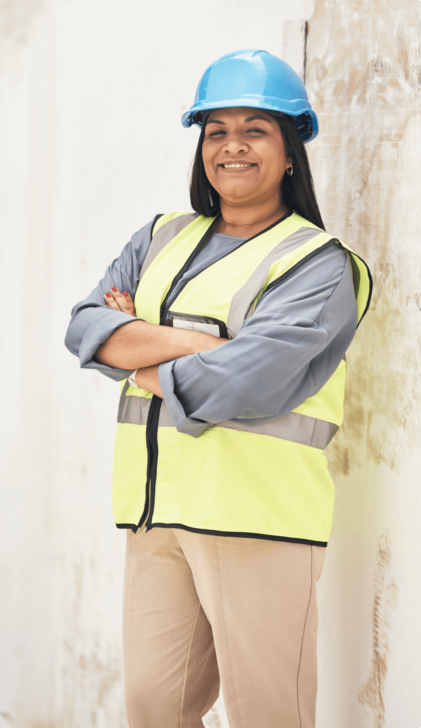 A woman wearing safety gear (hard hat, safety vest) crosses her arms in a two-thirds pose.
